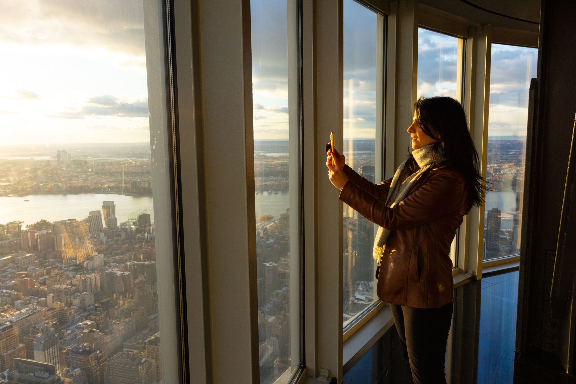 Jeune femme faisant une photo du coucher de soleil depuis le 102ème étage de l'Empire State Building à New York